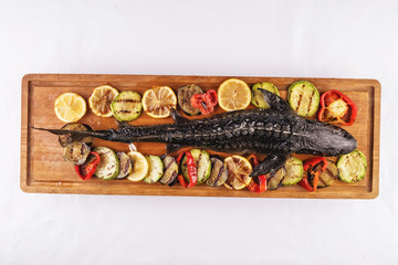  Seafood, Mediterranean cuisine. Baked sturgeon fish with grilled vegetables, tomatoes, lemon, zucchini and eggplants. Caucasian kitchen