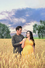 Pregnant girl and boyfriend stand in a wheat field at sunset