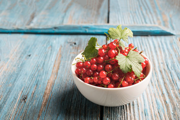 Fresh ripe red currant berry in a white cup on aged blue wooden background. Horizontal frame.
