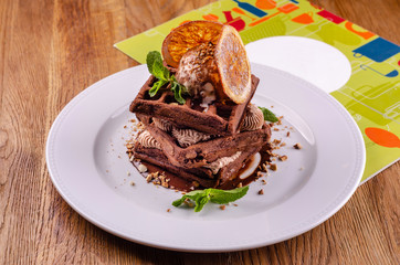 Plate of belgian chocolate waffles with slice orange, ice cream, caramel sauce and fresh mint on elegant white plate on wooden background. Close up. Top view dessert, copy space text