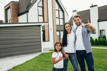 Happy heteroseksual family standing near their new house. Man holding keys from new apartment.