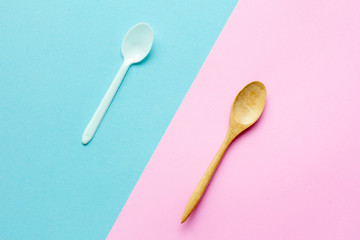 Flat lay wooden spoon with plastic spoon on pink and blue background.sustainable lifestyle and zero waste concept