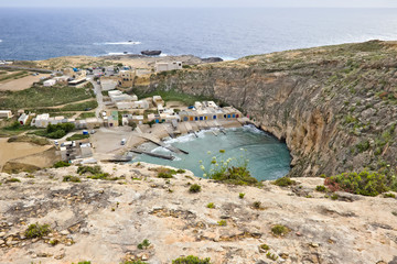 Inland sea (diving spot) with little houses in the background seen from above in gozo, Malta.