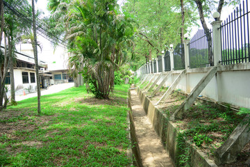the  cement  vent  near the metal fence  with the trees  ,palms and grass behind the buildings