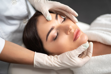 Young woman receiving face lifting massage at beauty salon