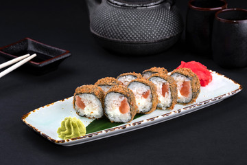 Closeup set of tempura fried sushi rolls with Philadelphia cheese, rice, salmon with chopsticks and soy on black background. Sushi menu. Japanese food and green tea teapot, copy space.