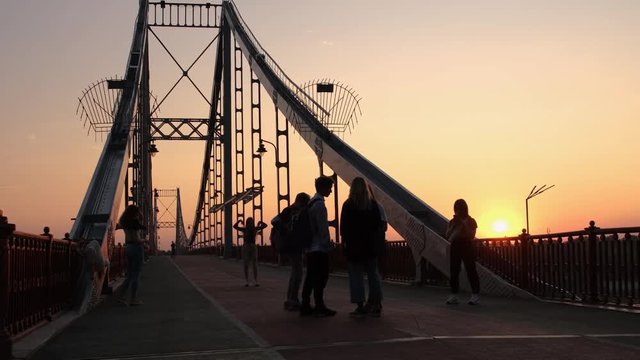 A group of teenagers are taking photos on the bridge during the sunrise time. Friends having fun at the dawn. Carefree school life concept 4k