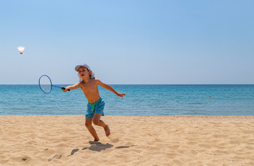 Naklejka na ściany i meble The child plays with a badminton racket and a shuttlecock on the beach. The concept of a family holiday. Copy space.