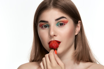 Closeup portrait of a beautiful young woman with bright color make-up holding strawberry near the face.