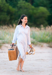 Attractive young woman walking on seacoast sand at sunset sunlight