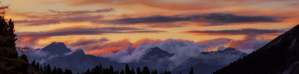 Fototapeta premium Wide angle panorama silhouette forest and mountain tops in red orange blue clouds gradient sunset