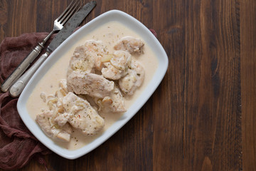 chicken with creamy sauce on dish on brown wooden background