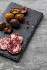 typical spanish smoked sausage salchichon and  boiled chestnuts on black board