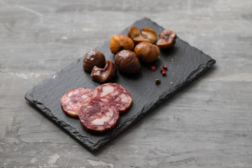 typical spanish smoked sausage salchichon and  boiled chestnuts on black board