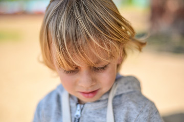 Portrait of a sad brooding boy against the sand. Lonely child walking on the beach. Blond baby looking into the distance.