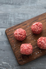 raw meatballs with pepper and salt on wooden board