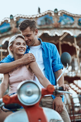 Loving man hugging shoulders of girlfriend in amusement park