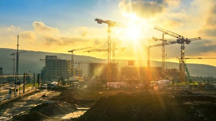 Time-lapse footage of a large construction site with several busy cranes in golden sunlight - Powered by Adobe