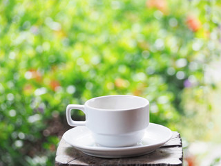white cup of coffee over green floral abstract blur background.