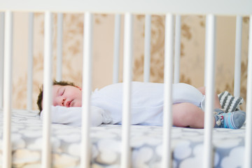 The baby sleeps in the crib. A charming baby sleeps in a crib for sleeping attached to the bed of the parents. A small child having a nap in the crib. Baby in the sun nursery