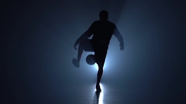 Football freestyle. Slow motion, football player stuffing ball on feet in twilight.