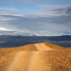 The road stretches into the distance mountains in the background. Kazakhstan. Big Charyn canyon. travel. copy space. square format.