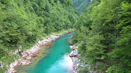 Flight of a quadcopter over a mountain's river canyon. We see the clear, transparent water of the river, it has the emerald color, the trees growing along the coast, and the mountains of Montenegro