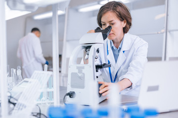 Female scientist works in the lab with the microscope in the front.