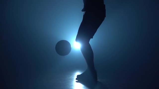Close-up football player's feet stuffing ball against blue spotlight. Slow motion