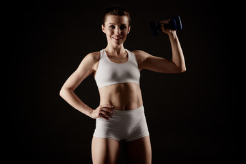 Fototapeta na wymiar Fit woman in sportswear shows her body off and lifts a dumbbell.