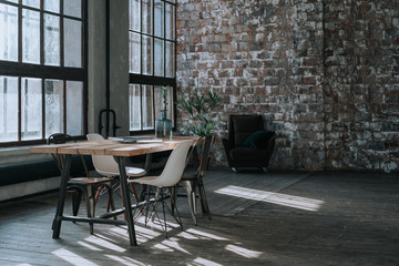 A simple loft-style interior with brick walls, a large window, a wooden table, chairs in different...