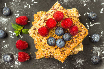Cookies with whole grains. Raspberry and blueberry berries with icing sugar on top. black background.