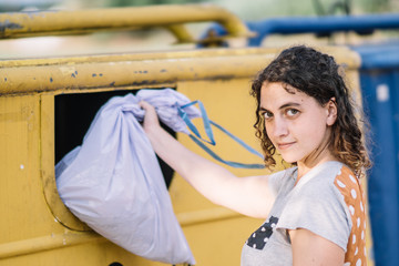 Woman looking at the camara throwing garbage in the yellow container.