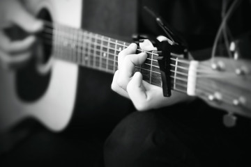 Fototapeta na wymiar Black and white image, where a person plays a melody on an acoustic six-string guitar, on the fretboard of which the strings are clamped with a capo.