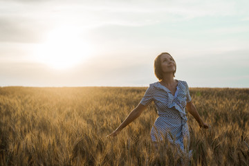 Middle age woman in a dress on a wheat field at sunset. Freedom, naturalness, nature concept.