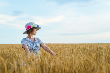 Naklejka na ściany i meble Free and happy woman in a flying dress and a hat on a wheat field. Freedom, joy concept.