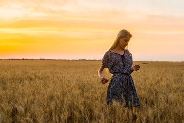 Girl teenager in a dress standing on a field at sunset.