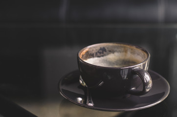 close up modern hot black coffee the cappuccino on dark background with coffee bubble foam pattern and texture in black cup looking and feel so delicious on glasses table in coffee shop.