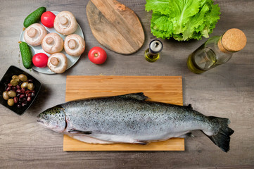 Top view keta fish, whole on the cutting board of the kitchen table next to olives tomatoes and mushrooms. Healthy sea food. Homemade cooking