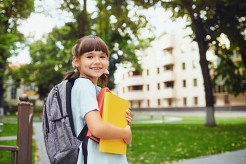 Happy little student girl with a backpack on her way to school.