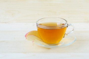 Hot tea in glass and slice red apple in disk on wooden background