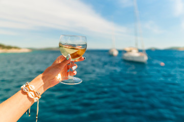 Woman holding glass of white wine over ocean background with yacht on background