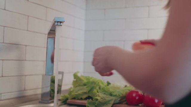 Woman is washing fresh organic red pepper under running water in kitchen sink