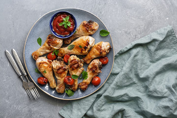 Grilled chicken drumstick with tomato sauce and greens on a gray background. Top view, flat lay, copy space.