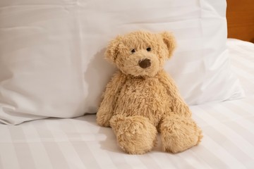 Cute teddy bear portrait in bed, sitting on the white pillow