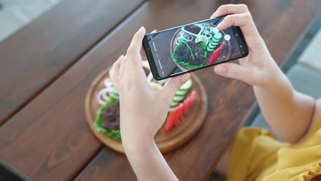 Food blogger hands using smartphone taking photo of beautiful beef steak on wood table inside the cafe to share on social media. Top view food photo. Lifistyle concept.