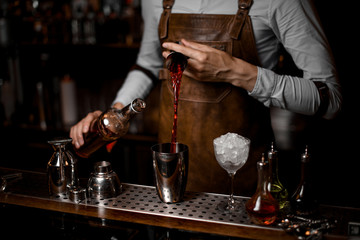 Fototapeta na wymiar Bartender pours cocktail from jigger to shaker