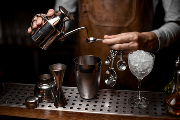 Fototapeta na wymiar Bartender prepares drink with kettle, spoon and shaker