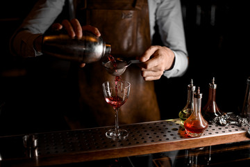 Bartender flows cocktail through sieve in glass