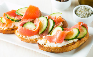 Salmon, cucumber and cream cheese bruschetta. Italian tapas, antipasti with vegetables, herbs and oil on grilled ciabatta and baguette bread. Sandwich.